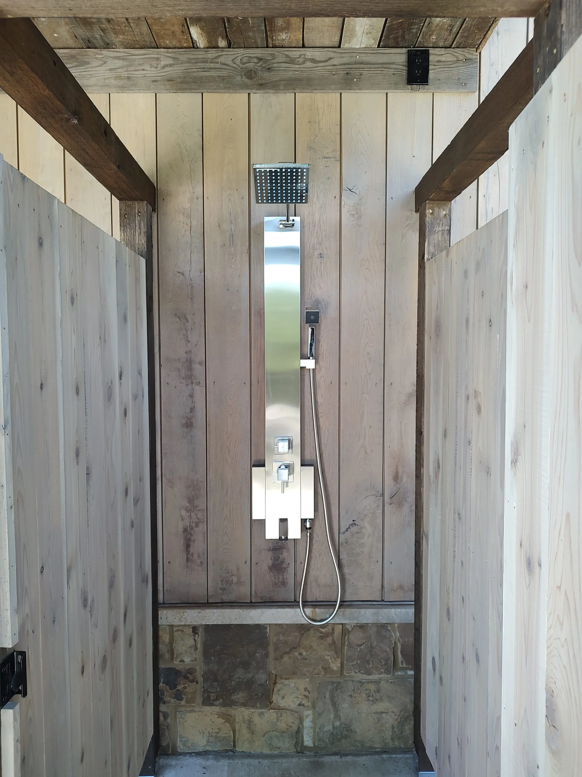 Rustic walk-in shower with a rain head and hand shower on weathered shiplap walls