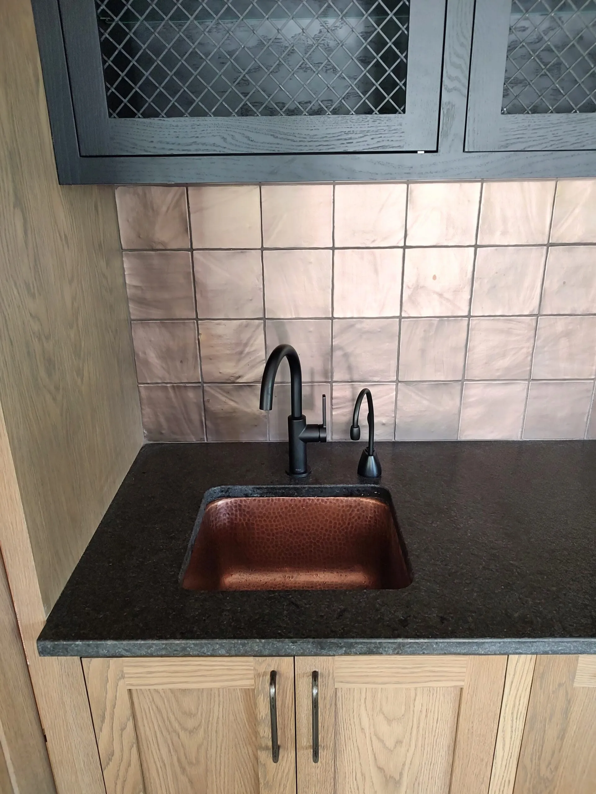 Hammered copper bar sink set in a black granite counter with a black faucet