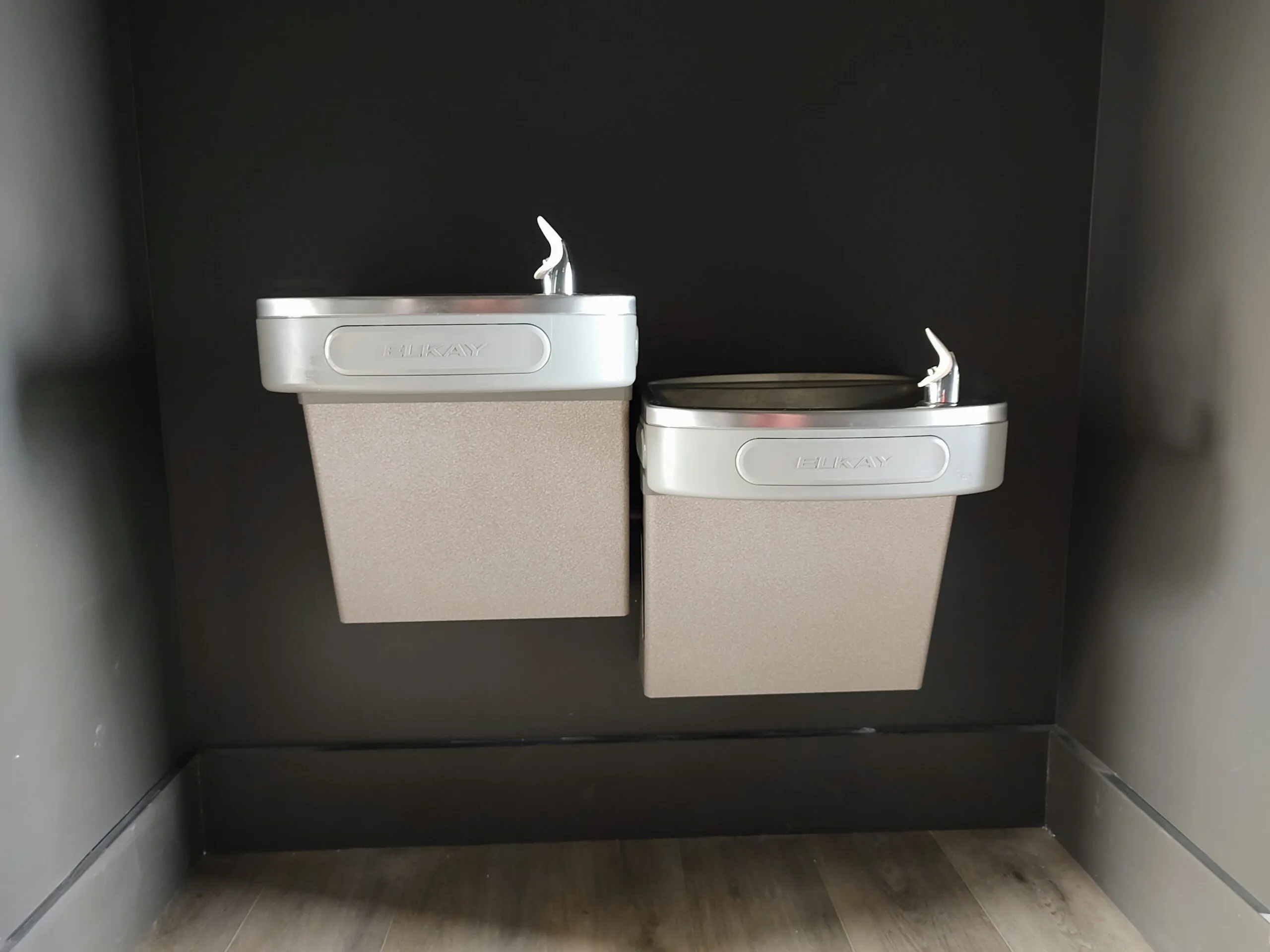 Dual height stainless steel drinking fountains on a dark accent wall