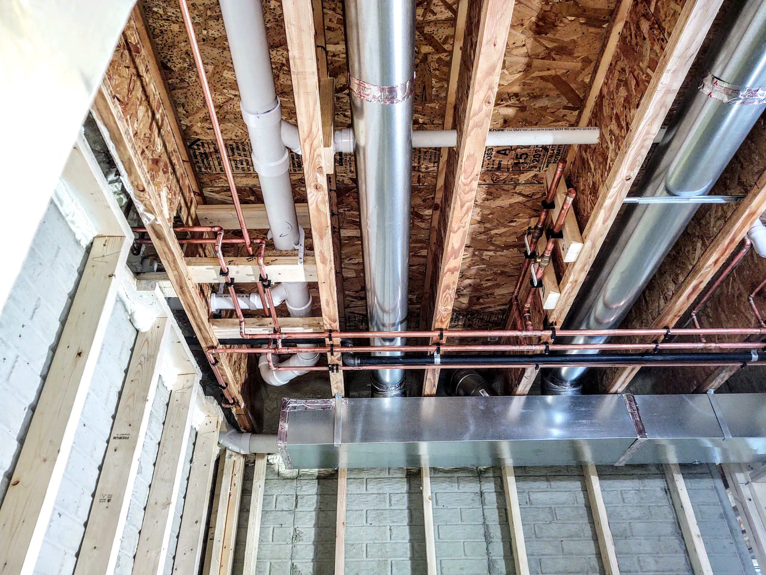 Copper supply lines and PVC waste piping run through new floor joists