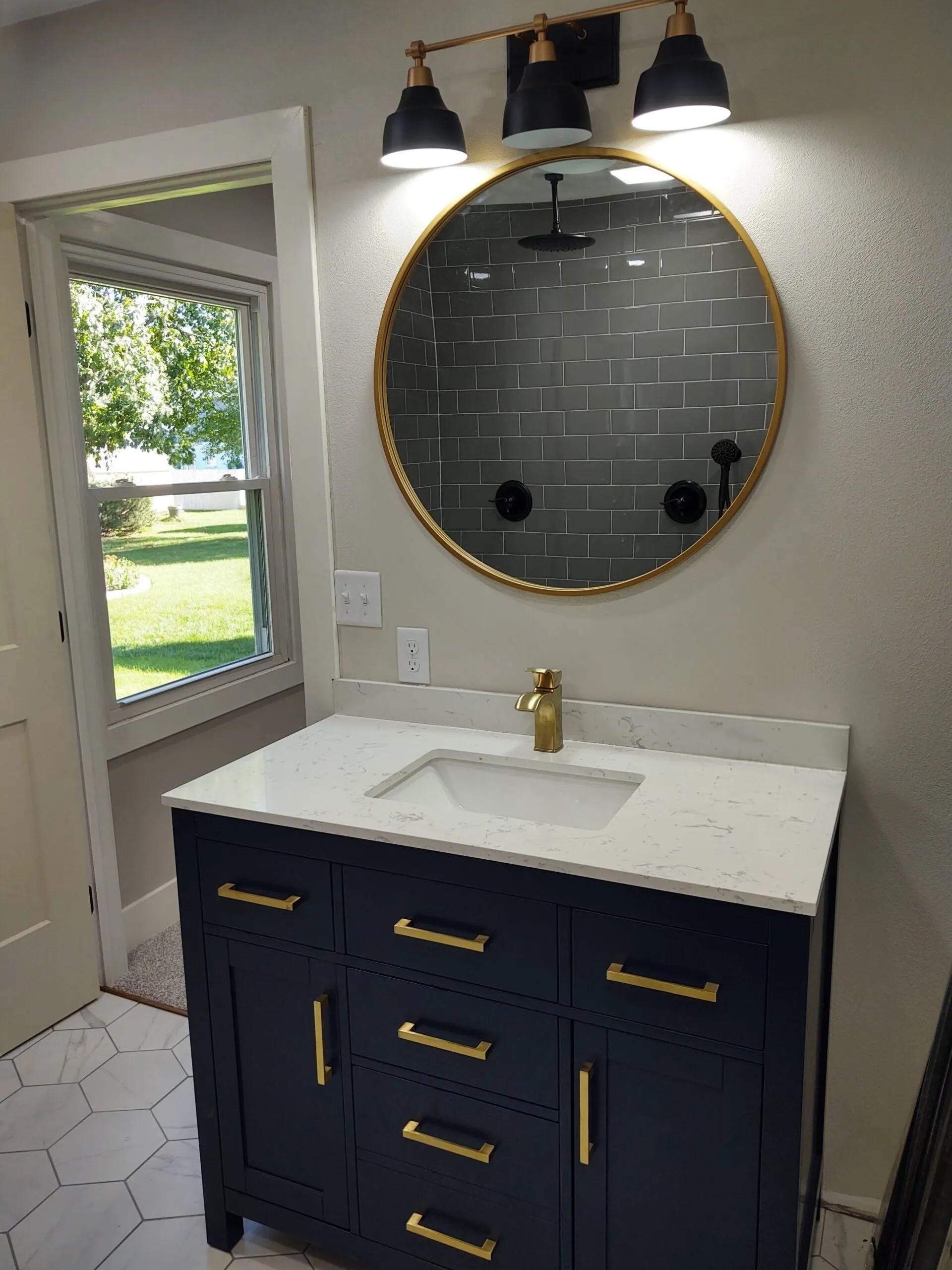 Navy vanity with a quartz top, gold faucet and round mirror over gray subway tile