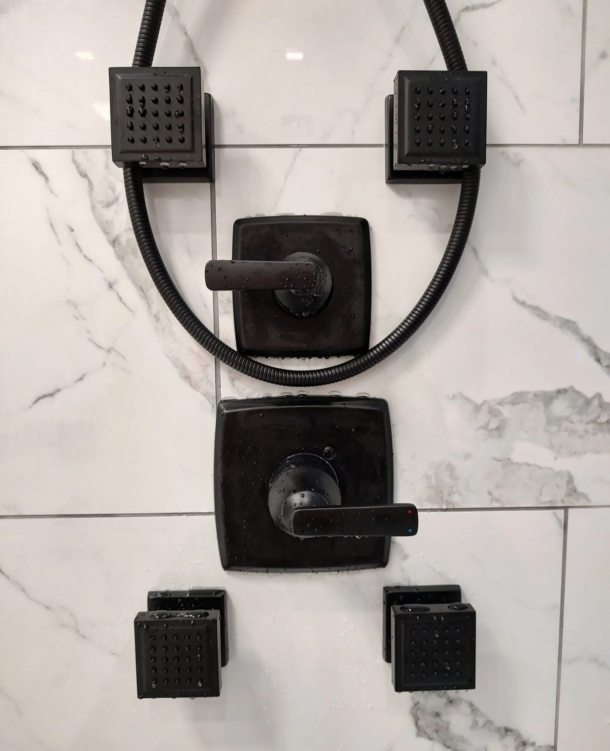 Black shower valve and body spray trim on large format marble tile