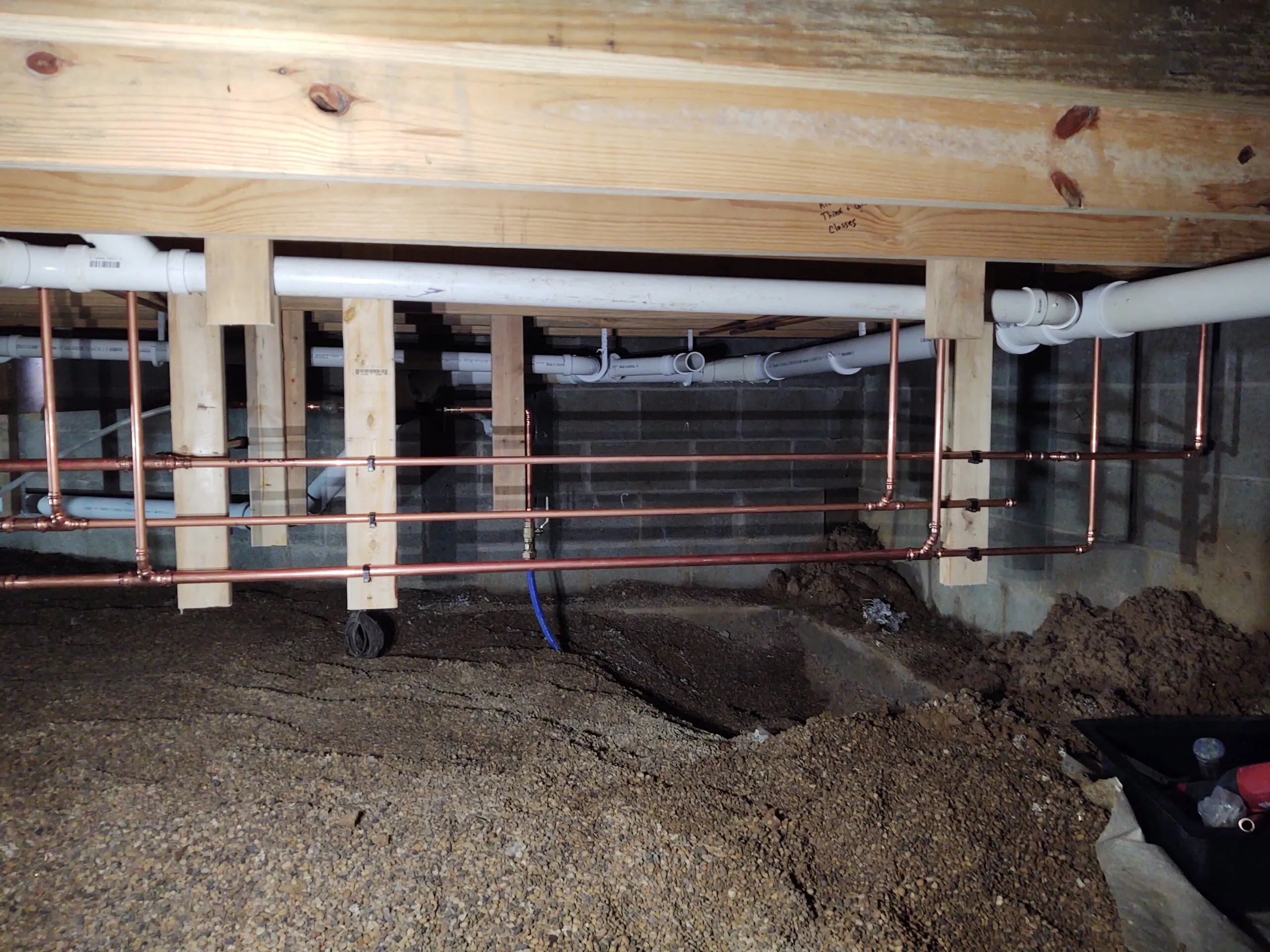 Copper water lines and PVC waste piping run through a crawl space